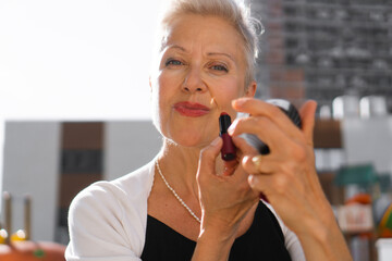 Close-up photo of a happy senior woman fixing her make-up on the street.