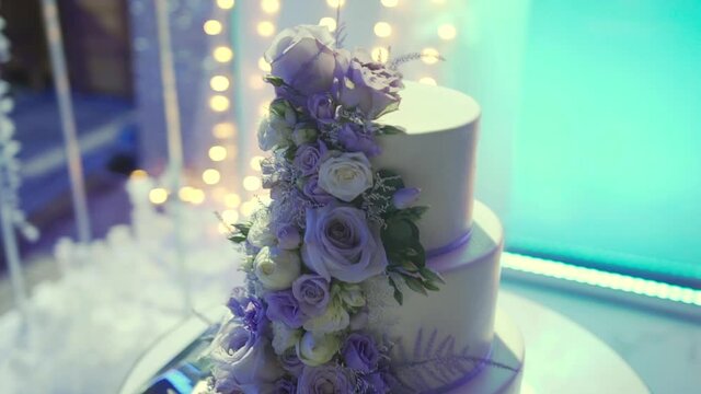 Exquisite wedding cake with three tiers stands on the background of the arch and decorated with fresh flowers. Next to cake from baked cakes and with cream there are cutlery - plate, knife and forks