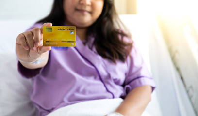 Asian fat woman patients lying in hospital patient bed and show creditcard mock up in hand.