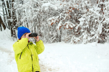 Fototapeta na wymiar Cute child explorer in snowy forest. Family vacation, snowy day and happy childhood. Kid looking to monocular.
