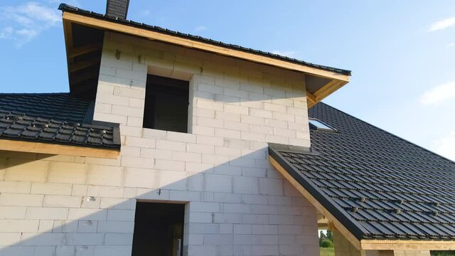 Unfinished frame of private house with aerated lightweight concrete walls and metal rooftop under construction.