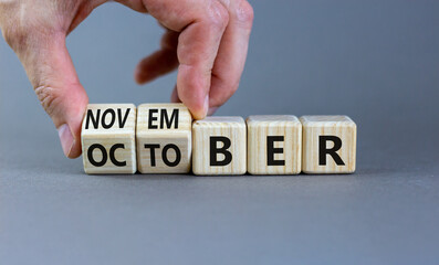 Symbol for the change from October to November. Businessman turns wooden cubes and changes the word 'October' to 'November'. Beautiful grey background, copy space. Happy November concept.