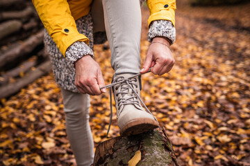 Woman tying shoelace on her hiking boot. Tourist is getting ready for autumn hike at forest...