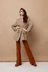 fashionable brunette in a coat, trousers and boots on a beige background in the studio