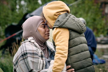 Happy middle-eastern mother in headscarf touching foreheads with daughter while finding her after escape from battlefield - obrazy, fototapety, plakaty