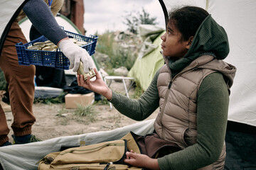 Social worker with box of preserves giving canned food To thankful middle-eastern refugee girl living in tent after escape - obrazy, fototapety, plakaty