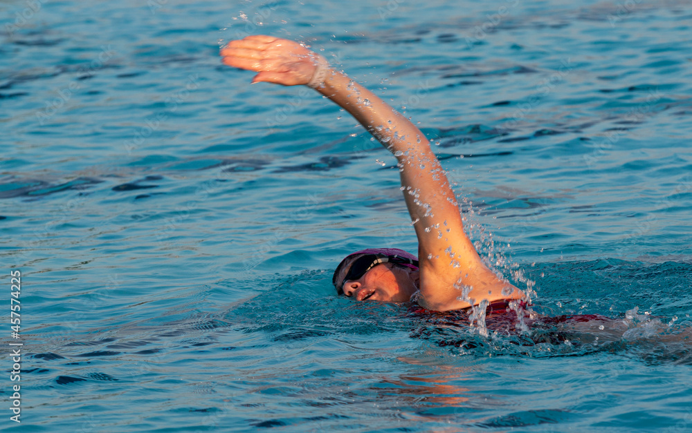 Wall mural Female freestyle swimming in a pool with the sun lighting up her face