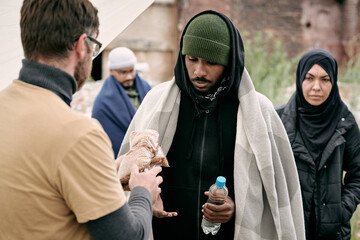 Social worker giving water and cereal to black man under plaid while providing food to refugees...