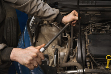 An auto mechanic unscrews the engine mount to replace the timing belt