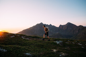 Fototapeta premium Young athletic man with backpack hike to reach summit of mountain at sunset. Cinematic beautiful adventure. Inspiring time spent outdoors. Explore norway in summer