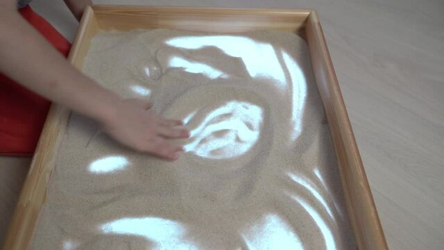 The child draws on the light table with his hands. Drawings in the sand. Art therapy. Fingers draw in the sand. The development of imagination. Patterns. The table is illuminated. Heart.