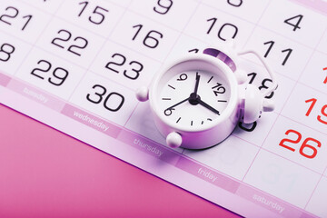 White alarm clock and calendar on a pink desktop background.