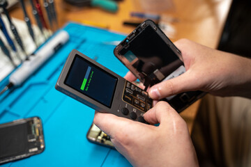 Hand technician setts up the smartphone screen with a programmer