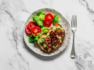 Delicious breakfast, brunch tapas - avocado, bacon sandwich and tomato lettuce salad on a light background, top view