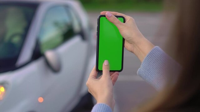 Girl with mobile green screen takes photo in parking. Car accident broken mirror