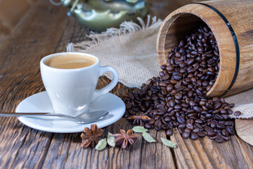 espresso cup with black roasted coffee beans in the background on an old wooden table top.