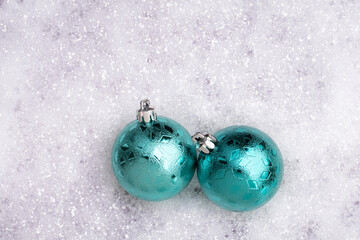 Teal colored Christmas ornaments rest in the snow
