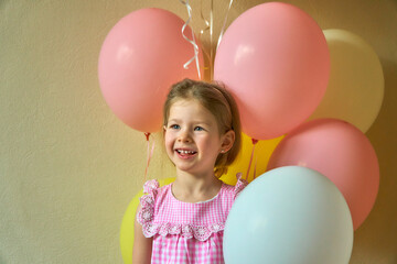Fototapeta na wymiar Little girl with balloons. Beautiful cute girl on a holiday. Happy cheerful child smiling and holding a lot of balloons. Delicate dress for a children's party.