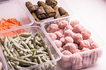Frozen vegetables and semi-finished meat products in plastic containers on a white plate. meatballs, dumplings, dolma in grape leaves, chopped beans and grated carrots