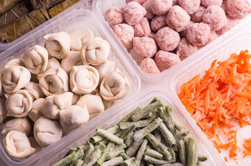 Frozen vegetables and semi-finished meat products in plastic containers on a white plate. meatballs, dumplings, chopped beans and grated carrots