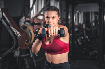 Fototapeta na wymiar Young woman with dumbbells in the gym. Portrait of young attractive woman in sport clothes holding weight dumbbell doing fitness workout