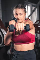 Young woman with dumbbells in the gym. Portrait of young attractive woman in sport clothes holding weight dumbbell doing fitness workout