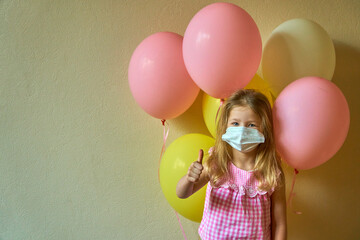 Holiday in quarantine. Party for children. Girl on a holiday with balloons in mask. Quarantine and isolation. Happy child jerking balloons on the background. Little cute girl smiling in medical mask.