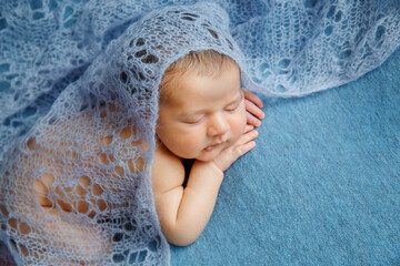 Sleeping newborn baby on a blue background covered by blanket. A few days from birth. Hands under the cheek.