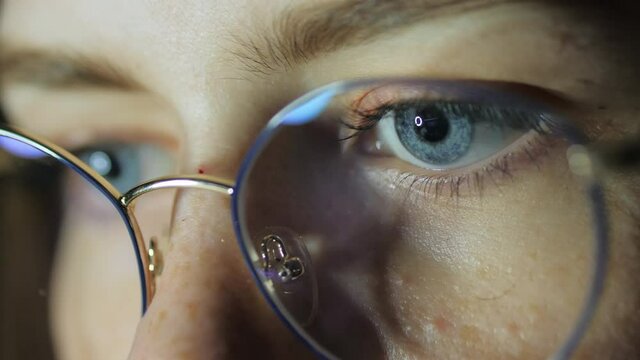 Close-up eyes of a teenage girl with glasses looks at the monitor, plays a game, reads, studies late at night
