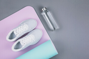 Top view of white sport shoes sneakers on pink blue yoga mat and eco glass water bottle over pastel...