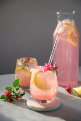 Refreshing beverage or lemonade with lemon and roses with sunny shadow on gray background. Vertical format. Close up.