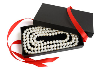 Natural pale pearl necklace in open black gift box with red satin ribbon, isolated on white