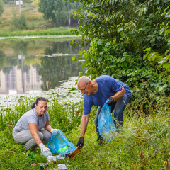 Naklejka na ściany i meble A woman and a man volunteers removes garbage from a green area dump.