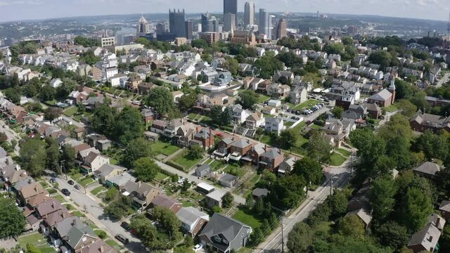 A slow forward motion and tilt up summer aerial establishing shot of a Mount Washington residential neighborhood overlooking the city of Pittsburgh.  	