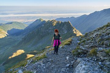 Naklejka na ściany i meble Woman hiker with backpack on a trail in the mountains