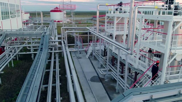 A drone at an oil refinery flies around tanks for storing and cleaning oil and gas. Oil and gas industry and work with natural gas. The worker makes a check, climbs the stairs to the gas storage.
