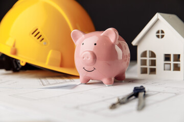 Yellow safety helmet and blue piggy bank with drawings and model of house. Building and investment concept