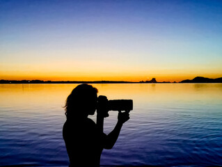 Silhouette of woman with photo camera on the beach during sunset.