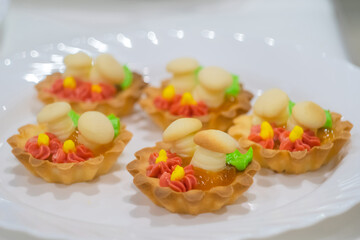 Close up: assortment of delicious fresh shortcrust tart cakes with cream and sweet mushrooms on white plate for sale at restaurant, cafe. Dessert, culinary and confectionery concept