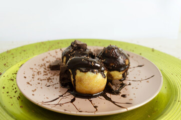 Profiteroles cubiertos de chocolate, hermoso emplatado mostrando un delicioso postre, vista de cerca, de fondo plato color verde brillante, fondo blanco