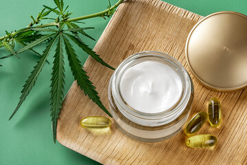 Hemp skin care moisturizer in a glass jar, few CBD oil capsules in a square wooden plate and fresh...