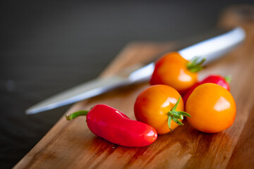 Small ripe tomatoes and red chilly peppers placed on wooden cutting board with a knife out of focus on the background