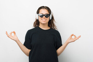 Smiling girl is listening to the music while meditating in a studio with white background.