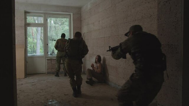 Anti-terrorist soldier eliminating terrorist in balaclava by knife while special forces squad entering room, covering area. Specialist providing psychological assistance to female hostage