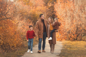 Happy family walking in the fall park. Portrait of a caucasian mother and father holding their children in beautiful outfits on a sunny autumn day in forest. Family lifestyle concept.