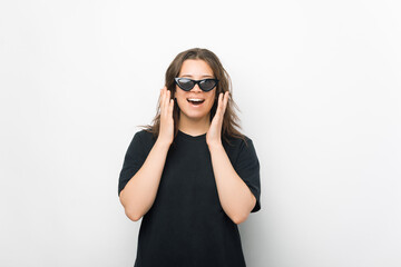 Young female wearing sunglasses is making the surprised gesture on white background.