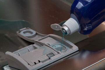 A person pours a rinse aid into the dishwasher.