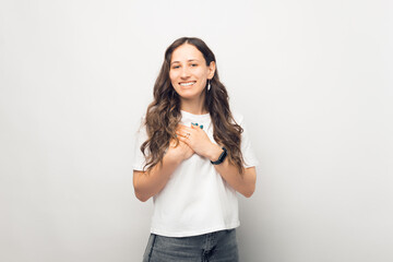 Young woman is showing compassion. Gesturing with hands over chest over white background.