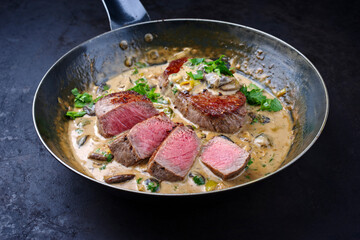 Traditional barbecue dry aged angus roast beef steak natural with mushrooms and onions in cream sauce served as close-up in a classic skillet