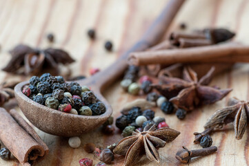 Grains of different peppers in a wooden spoon, anise stars, cinnamon sticks and cloves on a wooden table. Selective focus. Macro.